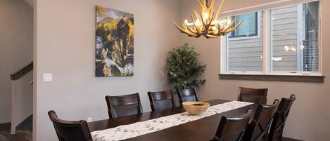 A dining room with a wooden table, chairs, a chandelier, a painting, and a window.