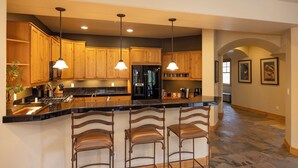 A spacious kitchen with wooden cabinets, a black refrigerator, and a bar area with three stools. - Cozy 3BR townhome in Durango with mountain views, perfect for families! (Durango)