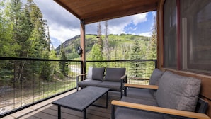 A wooden deck with outdoor furniture, a view of a forested mountain, and a large window. - Cozy 3BR townhome in Durango with mountain views, perfect for families! (Durango)