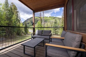 A wooden deck with outdoor furniture, a view of a forested mountain, and a large window. - Cozy 3BR townhome in Durango with mountain views, perfect for families! (Durango)