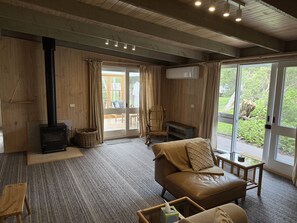 Ein gemütliches Wohnzimmer mit Kamin, einer Couch, einem Sessel und einer großen Schiebeglastür, die auf eine Terrasse im Freien führt.