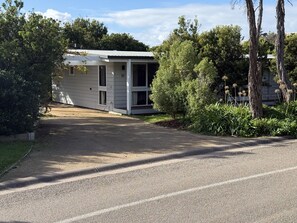 Ein Bungalow mit überdachter Veranda, umgeben von Bäumen und einer Schotterzufahrt.