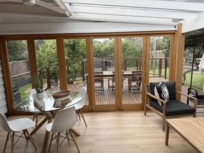 Eine überdachte Terrasse mit Glastür zum Außenbereich, ausgestattet mit Tisch, Stühlen und einer Couch.