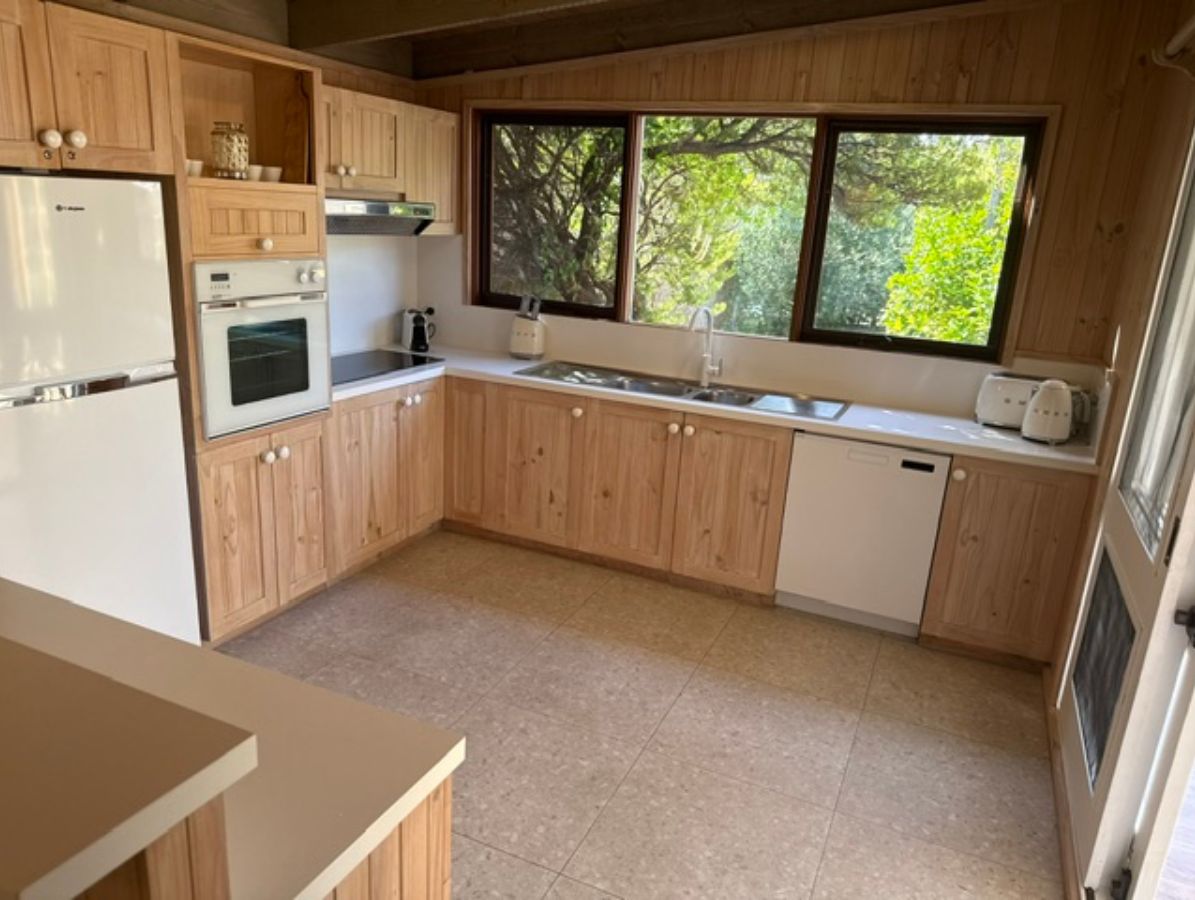 Une cuisine compacte avec des meubles en bois, un four encastré, un lave-vaisselle et une fenêtre donnant sur un espace verdoyant.
