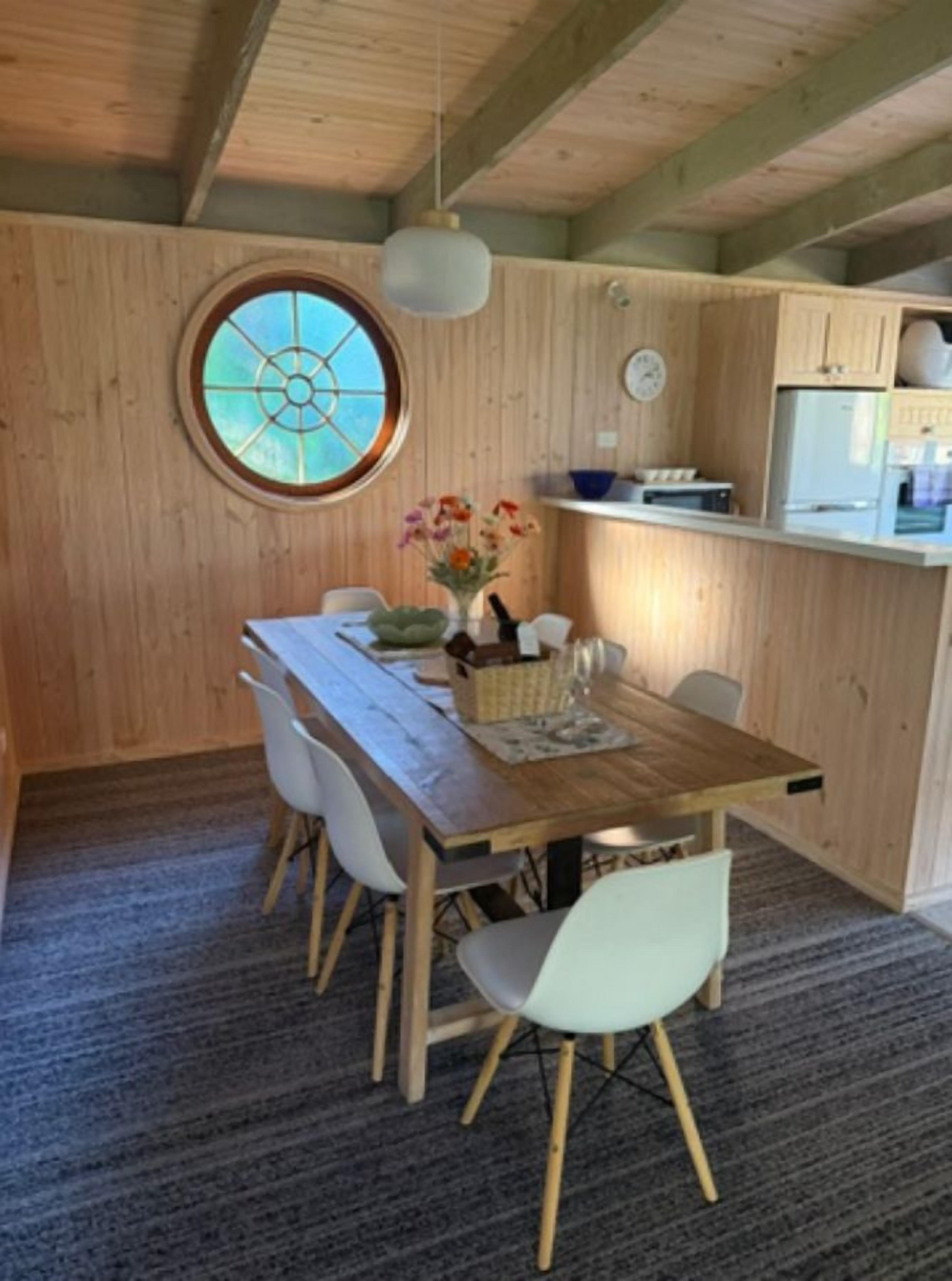 Une pièce aux murs lambrés, comprenant une table à manger, des chaises, une fenêtre ronde et un luminaire suspendu.