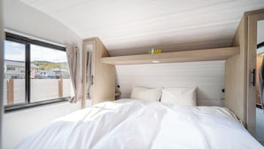 A bedroom with a bed, a window with curtains, a wooden ceiling, and a sign above the bed. - Glamping Trailer Lanikai (Awaji)