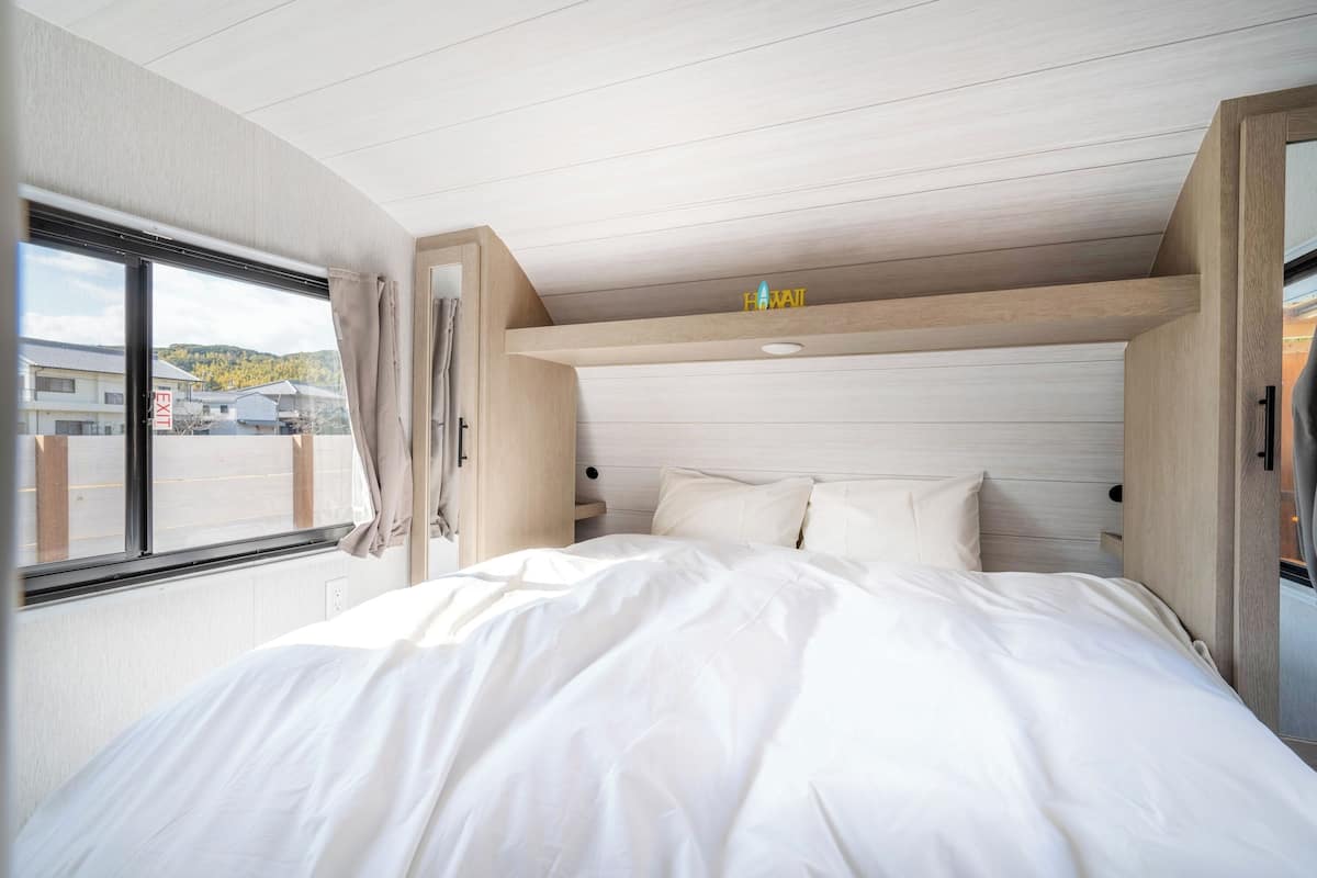 A bedroom with a bed, a window with curtains, a wooden ceiling, and a sign above the bed.