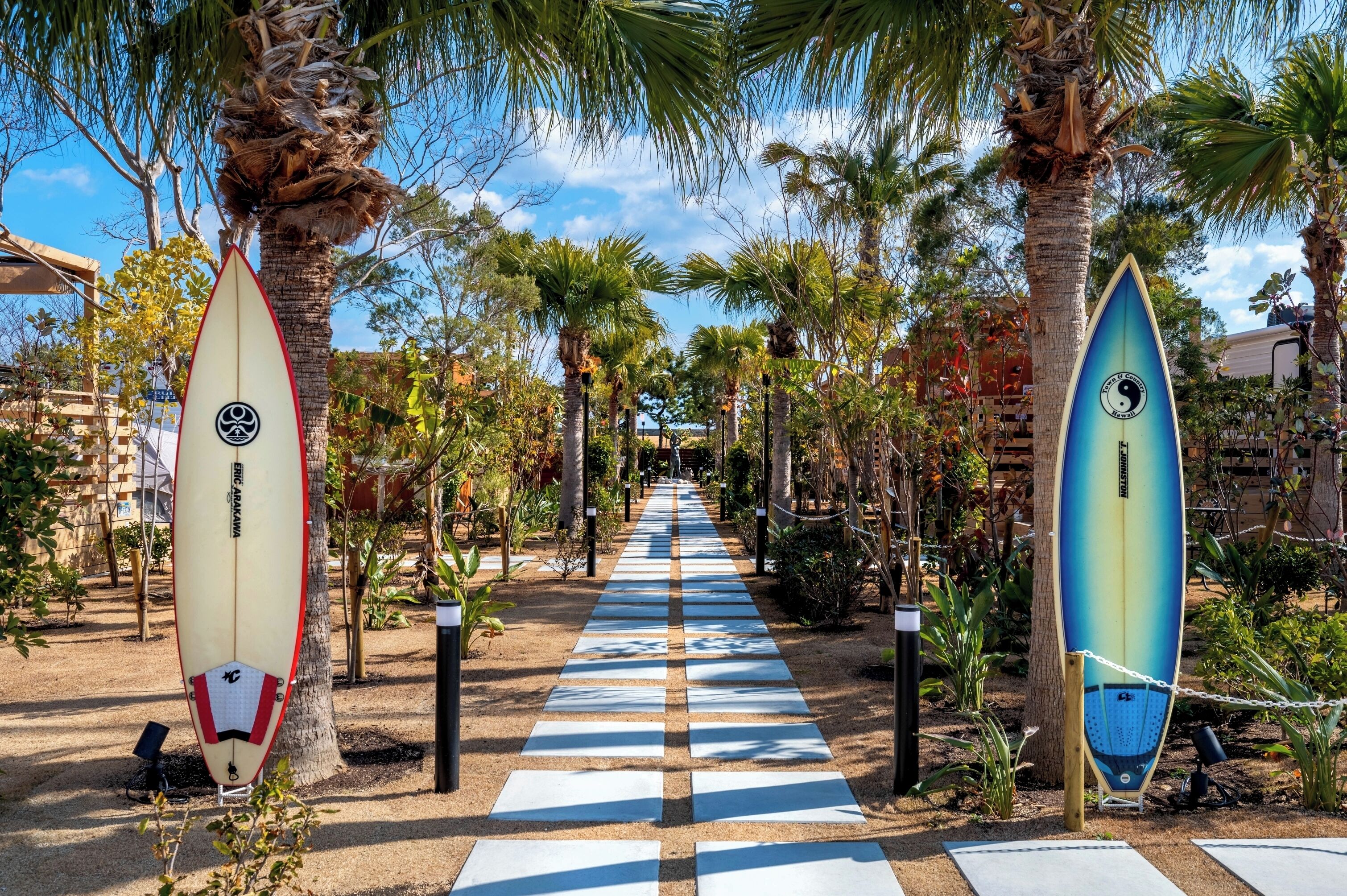 Un sentier bordé de palmiers et de planches de surf, qui mène à un bâtiment.