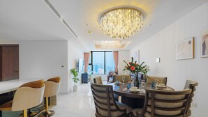 A modern dining area with a chandelier, a dining table set for four, and a view of the cityscape through large windows. - Imperial Suites by Kieu by Kita (Ho Chi Minh City)