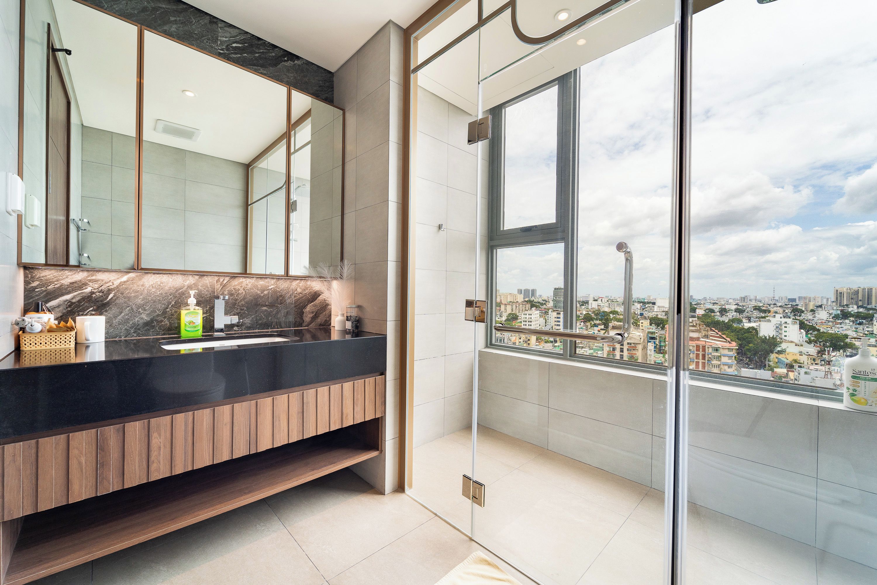 Un baño moderno con un espejo grande, una encimera negra y vistas a un paisaje urbano a través de un ventanal.