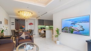A modern living room with a dining area, a kitchen, and a large painting of a coastal landscape. - Imperial Suites by Kieu by Kita (Ho Chi Minh City)