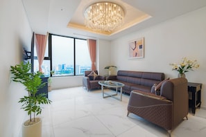 A modern living room with a large window, a chandelier, a sofa, a coffee table, and potted plants. - Imperial Suites by Kieu by Kita (Ho Chi Minh)
