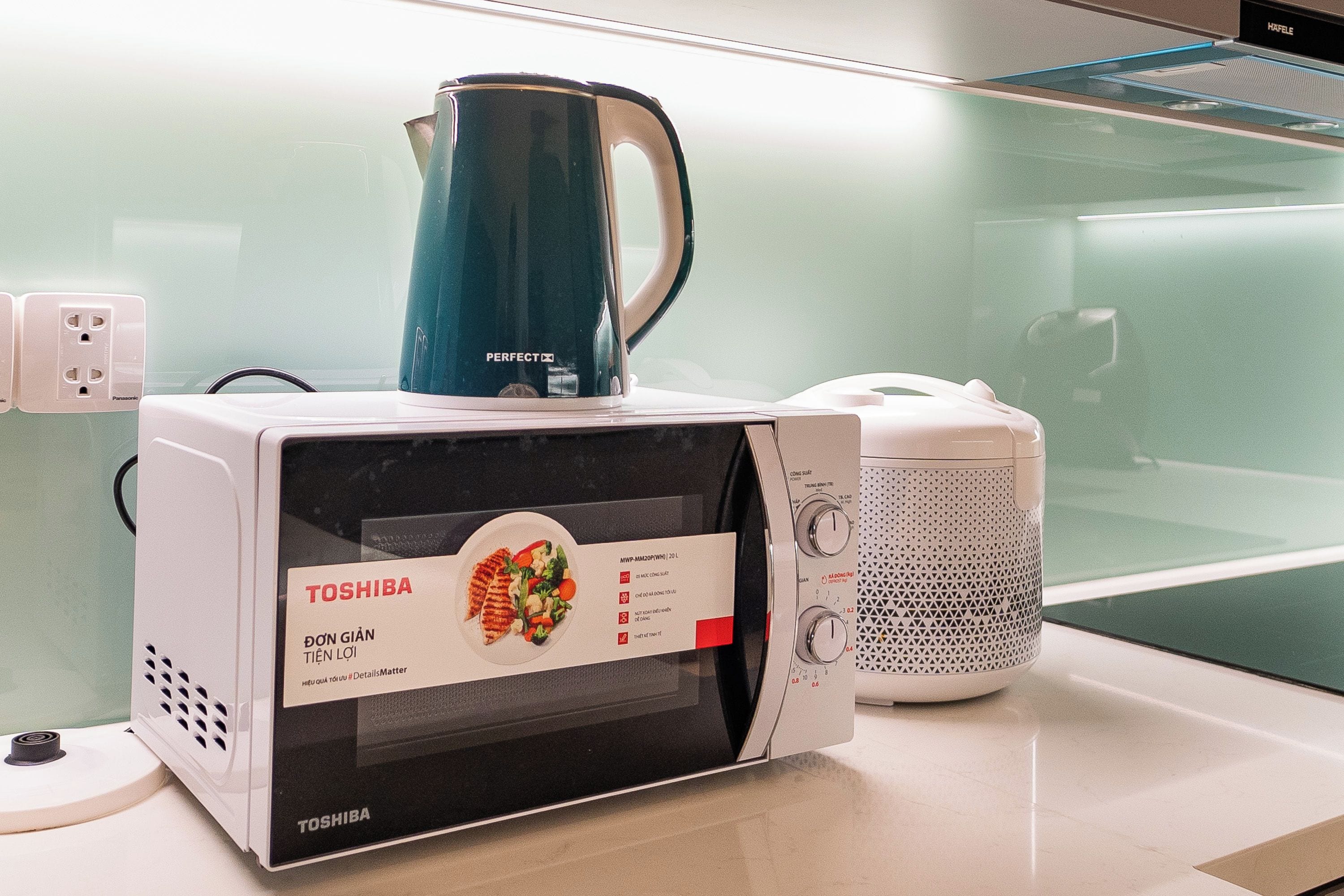 A kitchen with a Toshiba microwave, a kettle, and a white appliance with a red label.