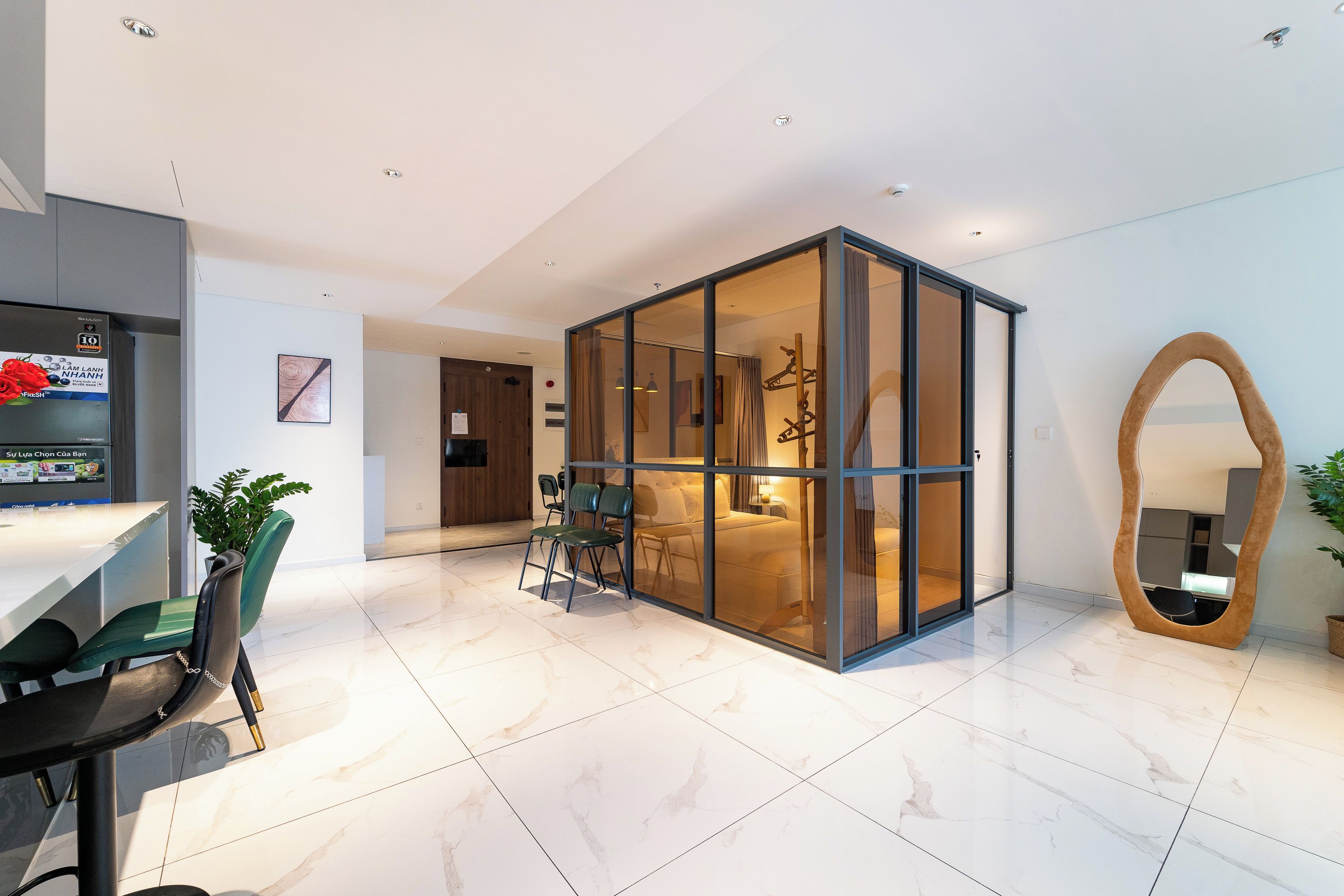 Une chambre d’hôtel moderne dotée d’une paroi en verre, d’un coin repas avec une table et des chaises, et d’un grand miroir.