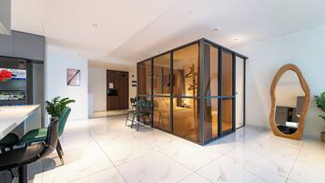 Une chambre d’hôtel moderne dotée d’une paroi en verre, d’un coin repas avec une table et des chaises, et d’un grand miroir.