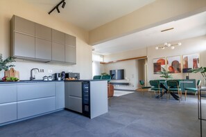 Eine moderne Küche mit grauen Schränken, einem eingebauten Geschirrspüler und einem Essbereich mit grünen Stühlen und einem Tisch.