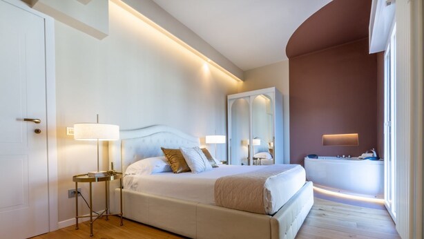 Un dormitorio moderno con una cama grande, lámparas de noche, un espejo y una bañera.
