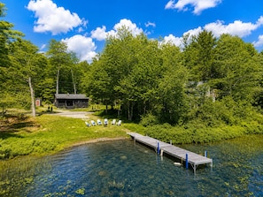 A lakeside cabin with a dock and chairs by the water. - Cozy Log Cabin by Phillips Lake, Pet Friendly, Near Acadia & Bangor (Dedham)