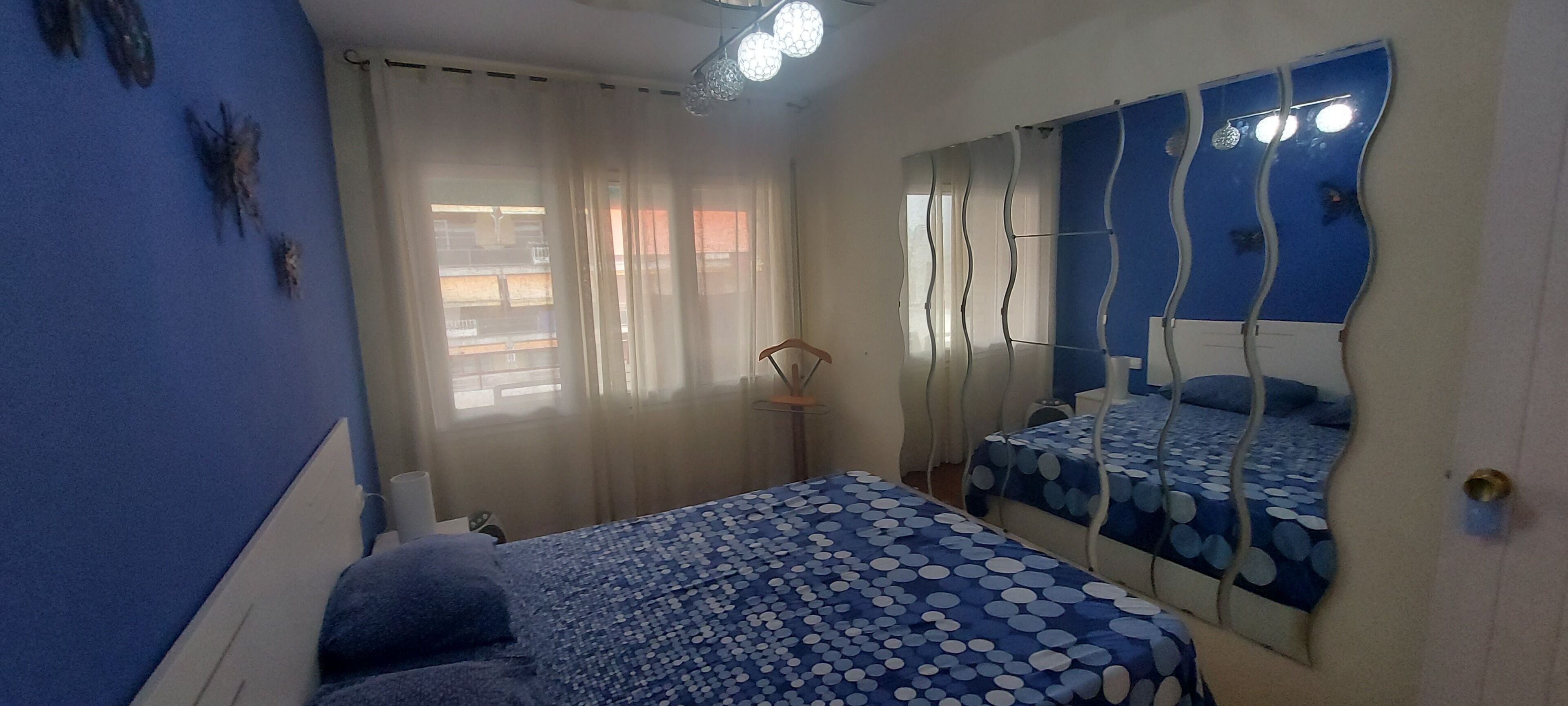 Ein Schlafzimmer mit einem Bett, einem Spiegel mit wellenförmigem Design und einem Fenster mit Vorhängen.