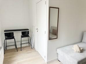 Una habitación con cama, espejo, escritorio y dos sillas, además de un radiador.
