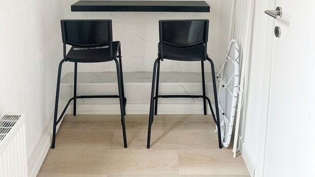 A small room with a white wall, a wooden floor, a black desk, two black chairs, and a white radiator. - Charming Studio Steps from City Center (Ghent)