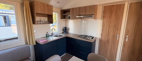 Una kitchenette compacta con estufa a gas, lavamanos y armarios de madera.
