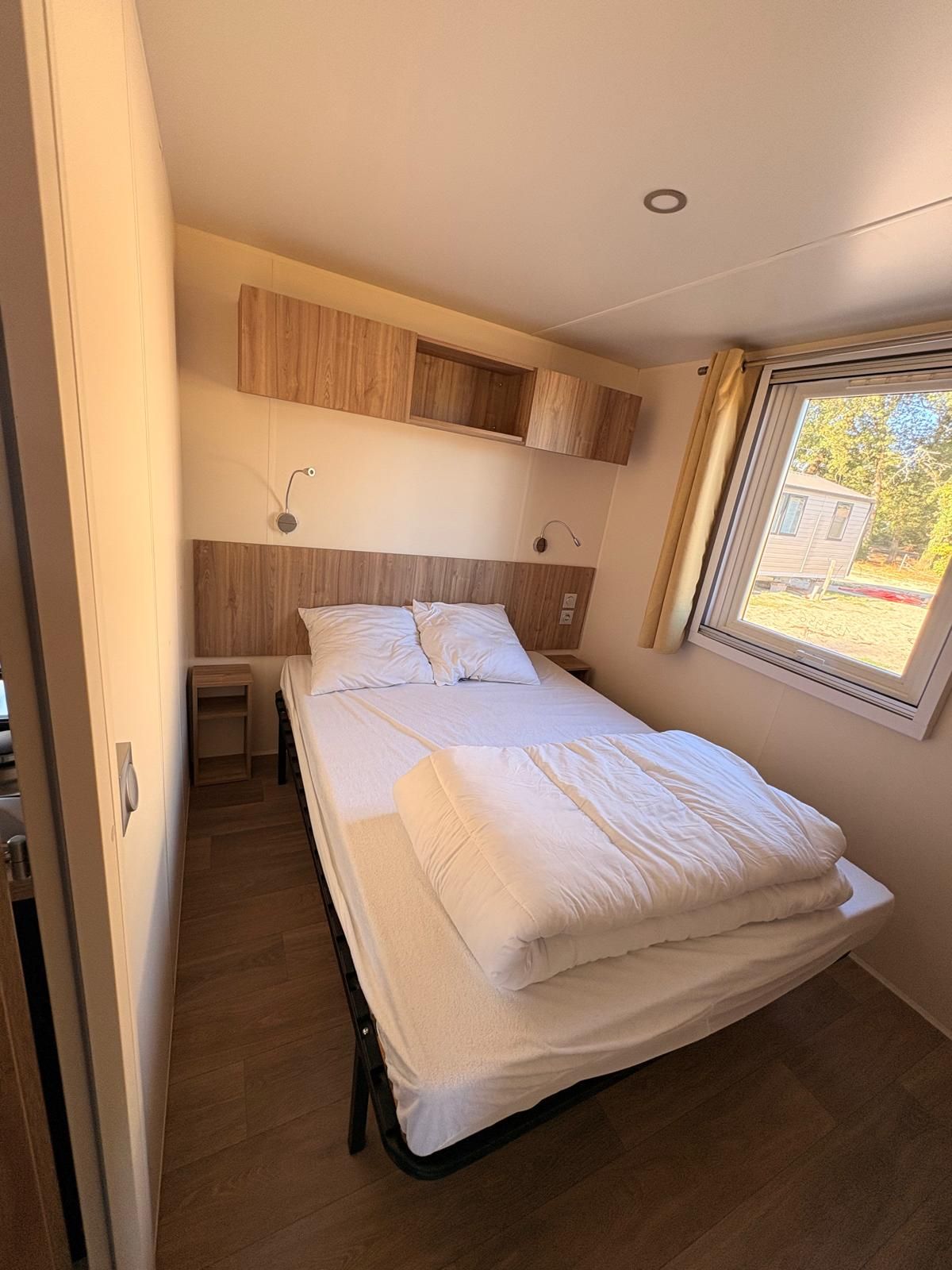 Un lit simple avec une tête de lit, une table de chevet et une fenêtre avec des rideaux.