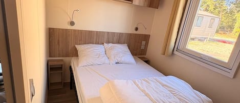 Un lit simple avec une tête de lit, une table de chevet et une fenêtre avec des rideaux.