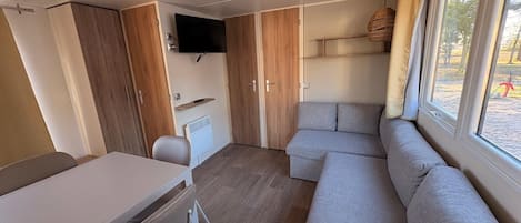 Un espacio habitable compacto con un sofá, una mesa, una silla y un televisor montado en la pared.