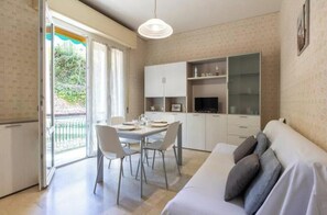 A compact living space with a dining area, kitchenette, and a sofa. - Hostdomus - Gassa d'amante (Finale Ligure)