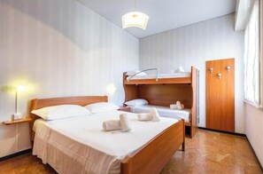 A room with a bunk bed, a single bed, bedside tables, a lamp, and a wardrobe. - Hostdomus - Gassa d'amante (Finale Ligure)