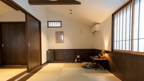 Een traditionele Japanse kamer met tatami vloerbedekking, een schuifdeur, een klein tafeltje met een lamp en een wandairconditioner.