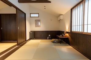 A traditional Japanese room with tatami flooring, a sliding door, a small table with a lamp, and a wall-mounted air conditioner. - Irodori Hotel DAIDAI (Fukuoka)