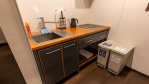 Een compacte kitchenette met een spoelbak, een waterkoker, een koffiezetapparaat en twee afvalbakken, gelabeld 'Niet brandbaar' en 'Brandbaar'.