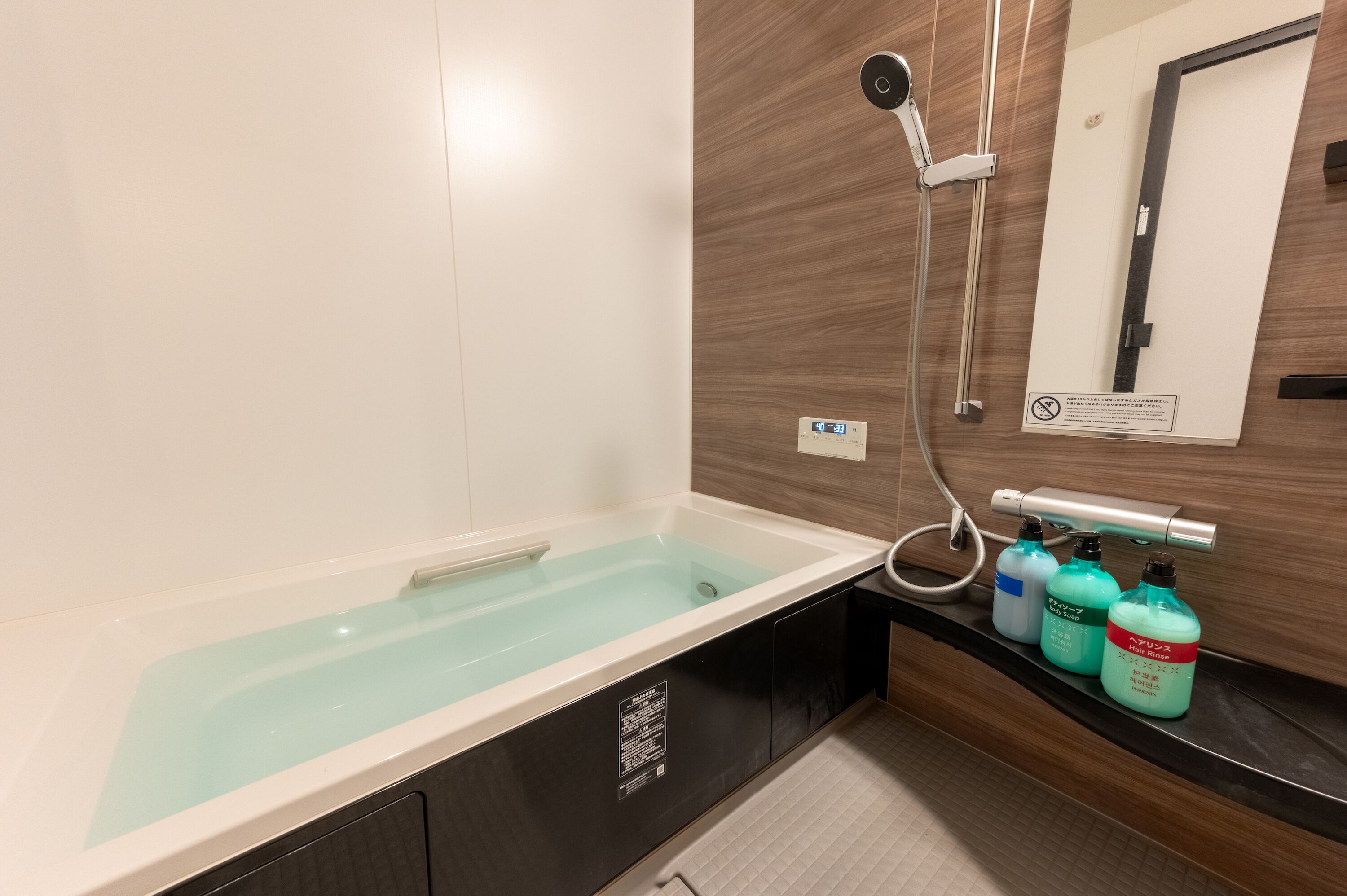 Une salle de bain équipée d’une baignoire, d’une douche et de trois flacons de savon liquide.