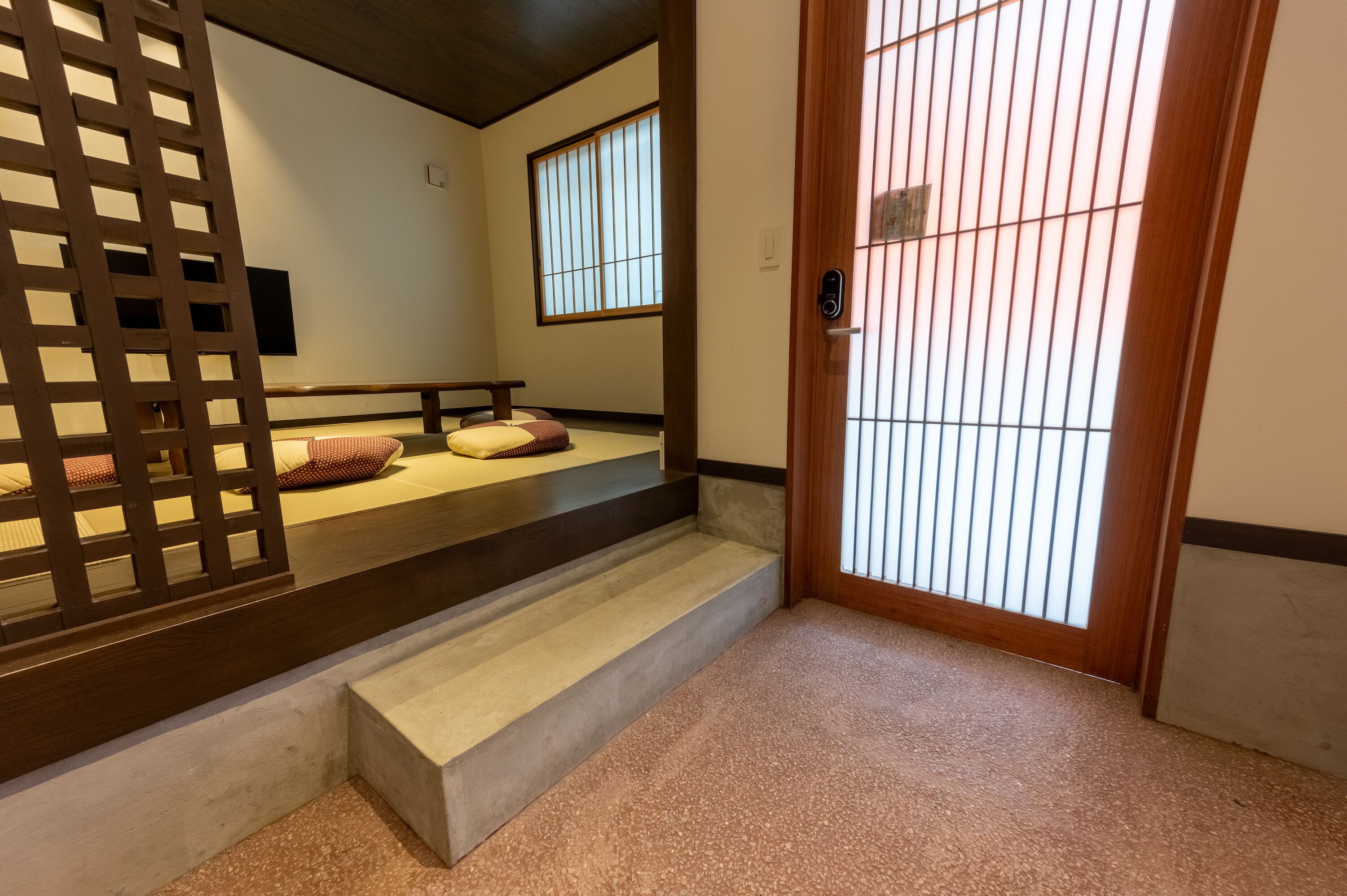 A traditional Japanese room with tatami flooring, a sliding door with vertical blinds, and a low wooden bench.