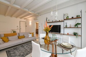 Ein modernes Wohnzimmer mit einem Glastisch, einem weißen Sofa und einem an der Wand befestigten Fernseher.