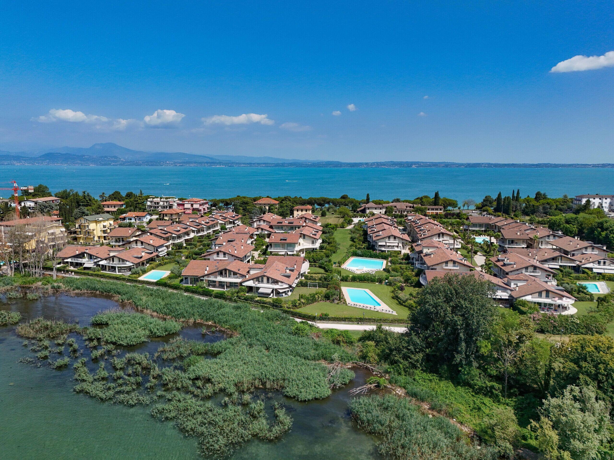 An aerial view of a coastal residential area with multiple houses, a swimming pool, and a body of water.