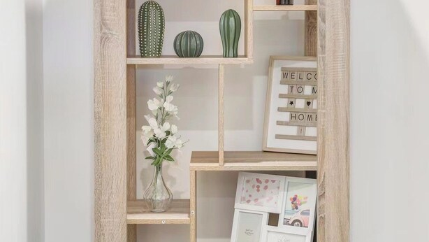 Una libreria in legno con diversi ripiani, alcuni dei quali contengono oggetti decorativi come un cactus, un vaso con fiori e un orsetto di peluche.