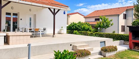 Um edifício residencial com varanda coberta, área de estar externa e escadas que levam à entrada.