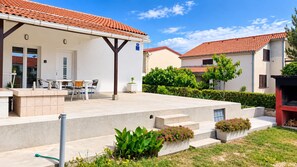 Ein Wohngebäude mit überdachter Terrasse, Sitzgelegenheiten im Freien und einem kleinen Garten.