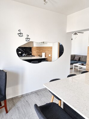 Ein modernes Interieur mit Essbereich, einer durch einen Spiegel sichtbaren Küche und einer Sitzecke mit einer Couch.