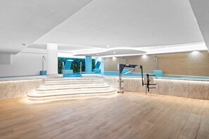 A modern indoor pool area with a marble staircase leading to the pool, a lounge area with blue chairs, and a ceiling-mounted water feature. - Casa Banzu | Pool - Terrace - Gym (Mijas)