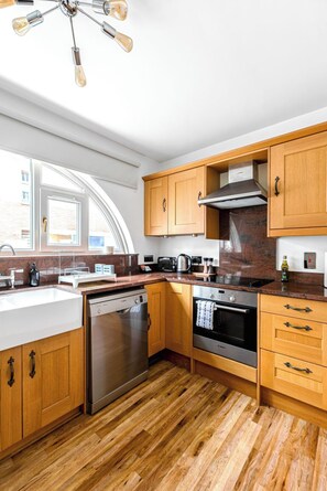 Eine moderne Küche mit Holzausstattung, einer Spülmaschine, einem Backofen und einem Einbauherd.