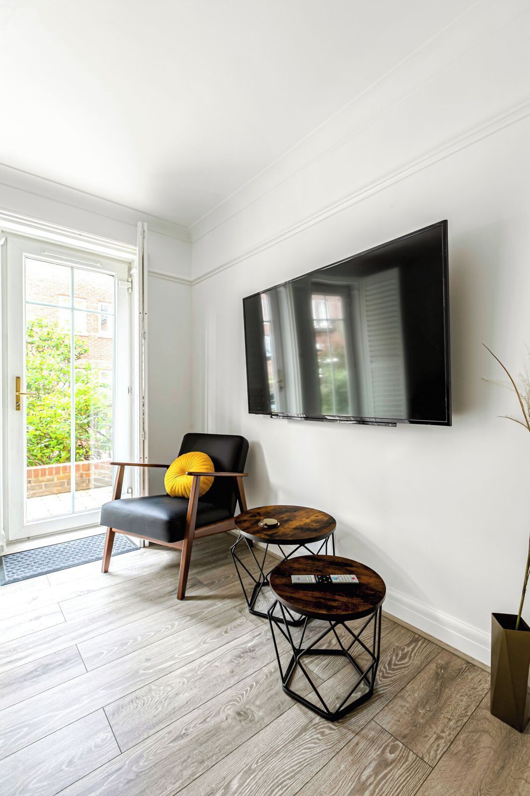 A modern living room with a black leather chair, a round wooden coffee table, and a flat-screen TV mounted on the wall.