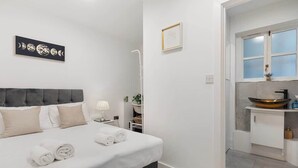 Ett hotellrum med en säng, ett nattduksbord, en lampa, en inramad tavla och ett badrum med handfat och spegel.