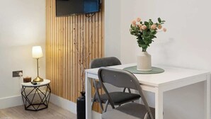 Ett modernt rum med en väggpanel i trä, en platt-TV, en väggklocka, ett matbord med stolar, en lampa och en vas med blommor.