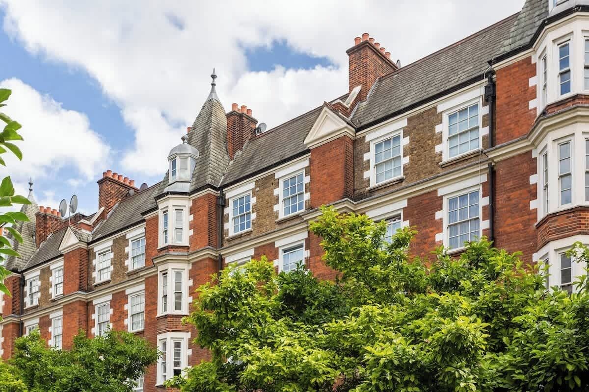 A row of red brick townhouses with white window frames, a central tower, and a clear sky.