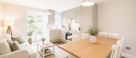 A modern kitchen with white cabinets, a wooden dining table, and white chairs.