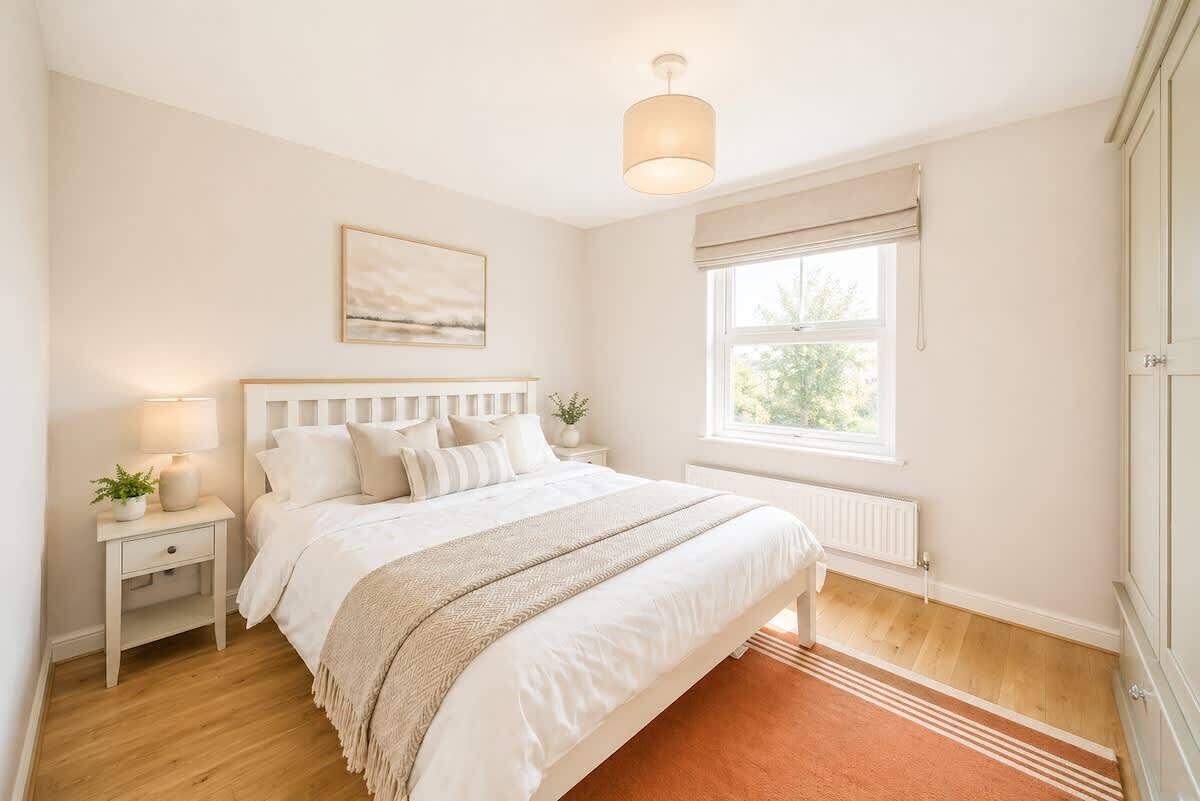 Une chambre à coucher comprenant un lit, une table de chevet, une lampe, une fenêtre et une œuvre d’art.